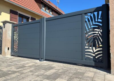 Portail aluminium anthracite à décor de palmes découpé, entre deux piliers enduits