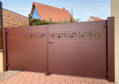 Portail battant aluminium brun-rouge à bandeau ajouré, au bout d'une entrée pavée