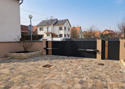 Portail battant motorisé anthracite à inserts couleur bois, vu depuis une cour pavée