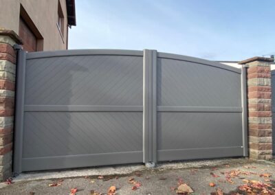 Portail aluminium gris cintré à panneaux rainurés en chevrons, entre piliers en grès